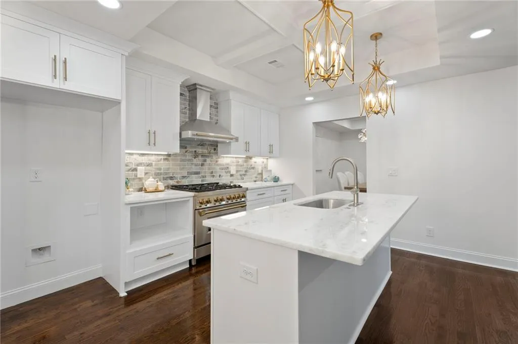 White cabinetry, stone tile backsplash, stainless steel range with hood, island with integrated sink, and dark wood-finish flooring