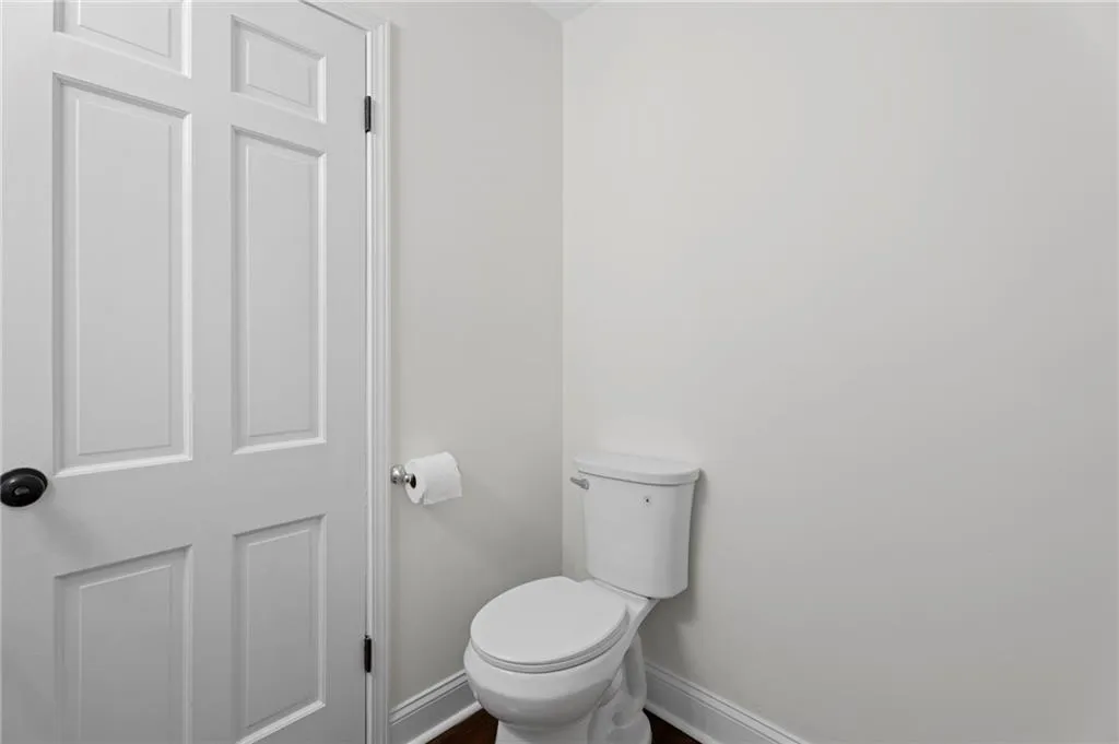 White paneled door with a matte black knob, white walls, and a built-in toilet