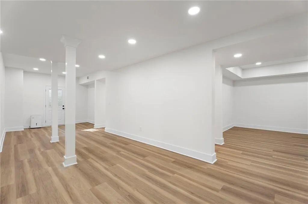 Spacious open-concept basement featuring gleaming wood-finish flooring throughout, recessed ceiling lighting, and structural support columns