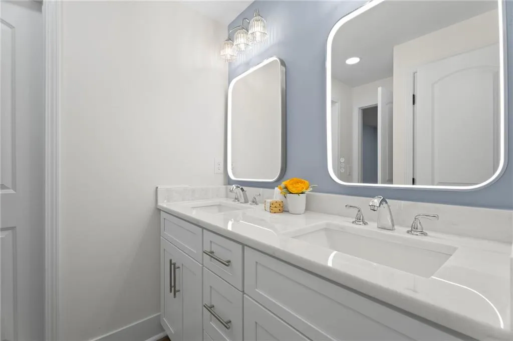 Dual vanity with white cabinetry, polished chrome hardware, integrated sinks, and backlit mirrors