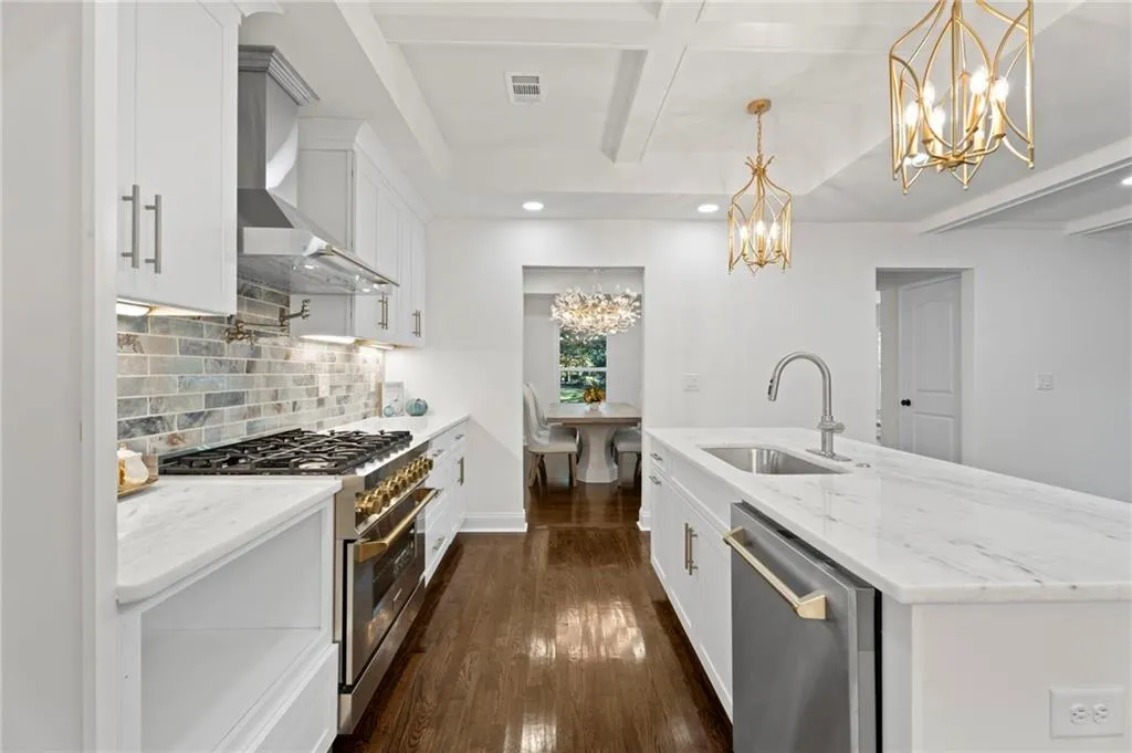 Kitchen featuring white cabinetry, wood-finish flooring, an expansive island with a built-in sink, a professional-grade range, and a coffered ceiling