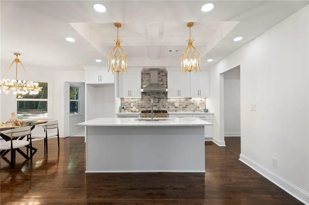 Spacious kitchen featuring a central island with a sink, white cabinetry, integrated stainless steel appliances, and wood-finish flooring