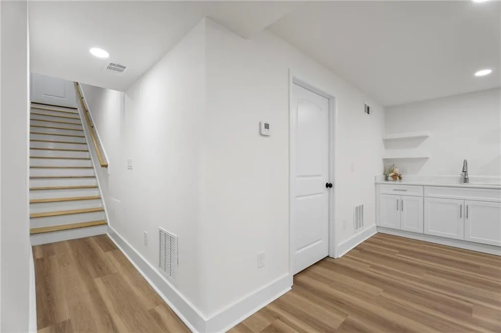 White painted walls, wood-finish flooring, recessed lighting, built-in shelving, and a wet bar with a stainless steel sink