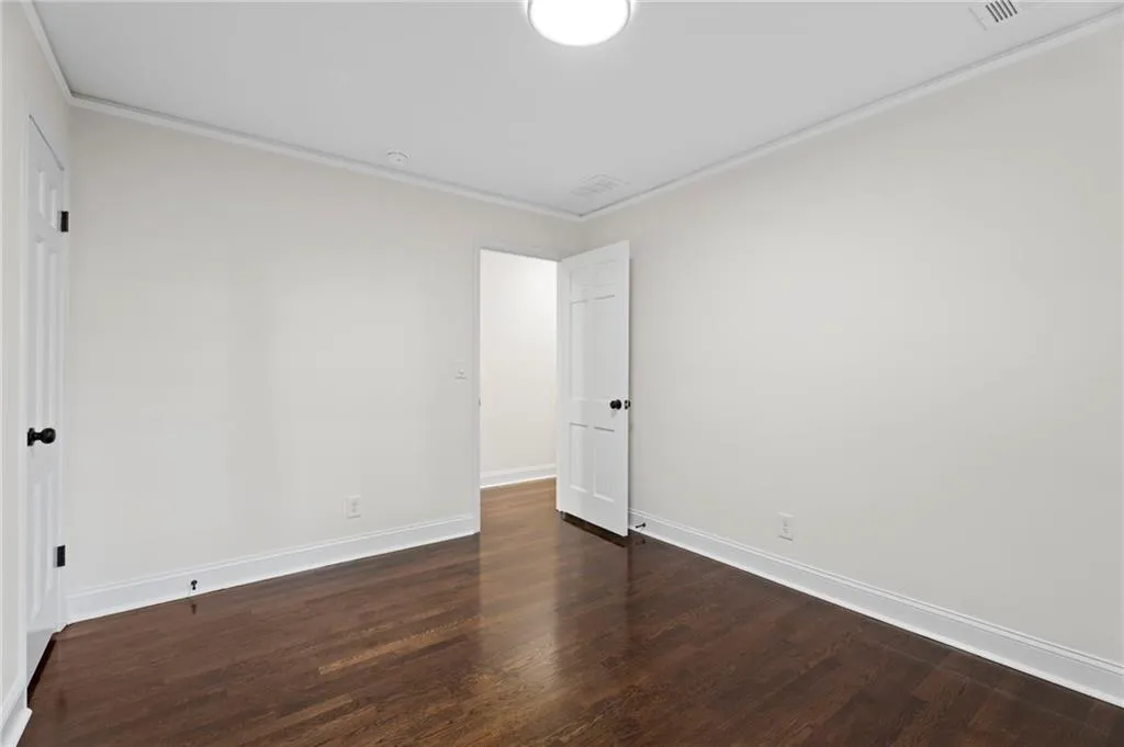 Hardwood flooring, crown molding, white walls, white trim, and a white paneled door