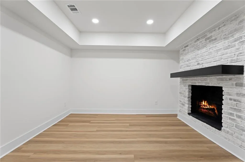 Whitewashed brick fireplace with a dark mantel, recessed lighting, wood-finish flooring, and crown molding