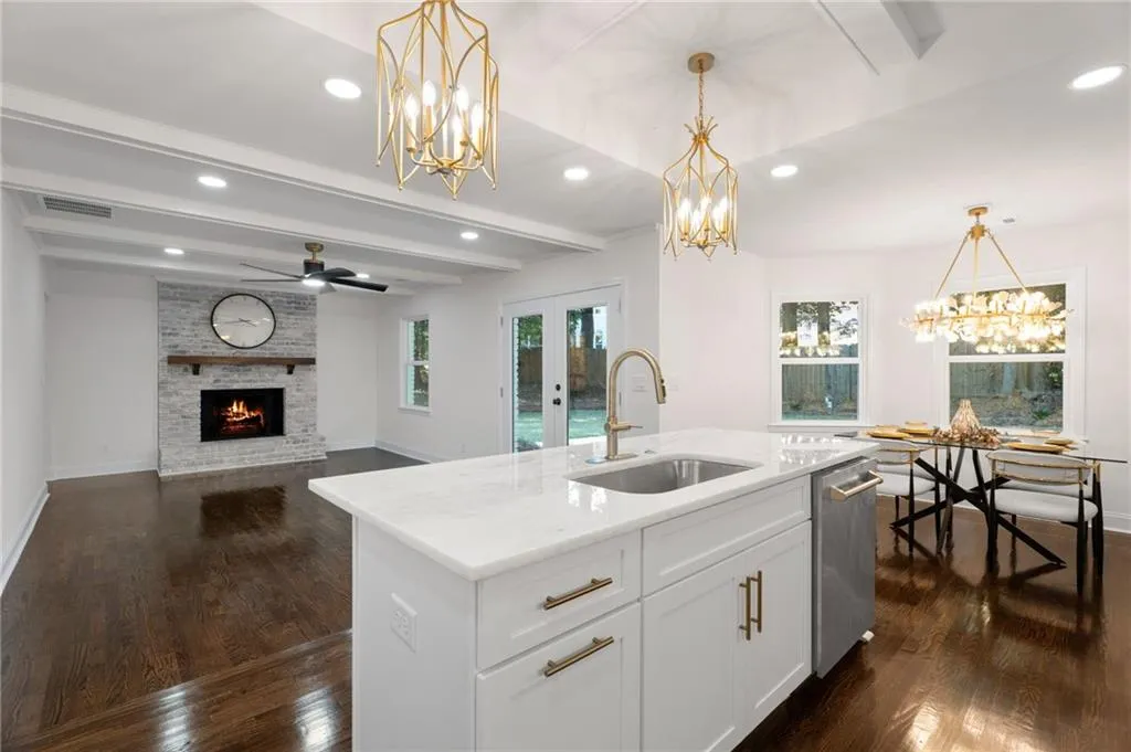 Open-concept kitchen and living area featuring a large white island with waterfall countertop and brass hardware, professional-grade stainless steel appliances, pendant lighting with brass fixtures, dark wood-finish flooring throughout, and a gas fireplace with white shiplap surround and integrated shelving
