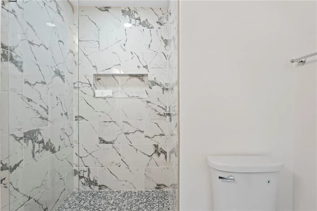 Walk-in shower with marble-look tile, mosaic tile shower pan, recessed shower niche, and glass enclosure