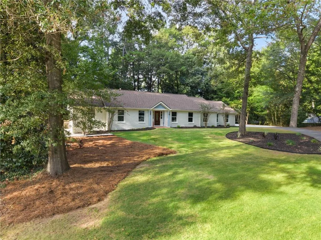Ranch-style residence featuring a prominent front lawn, mature trees, and a dark asphalt driveway