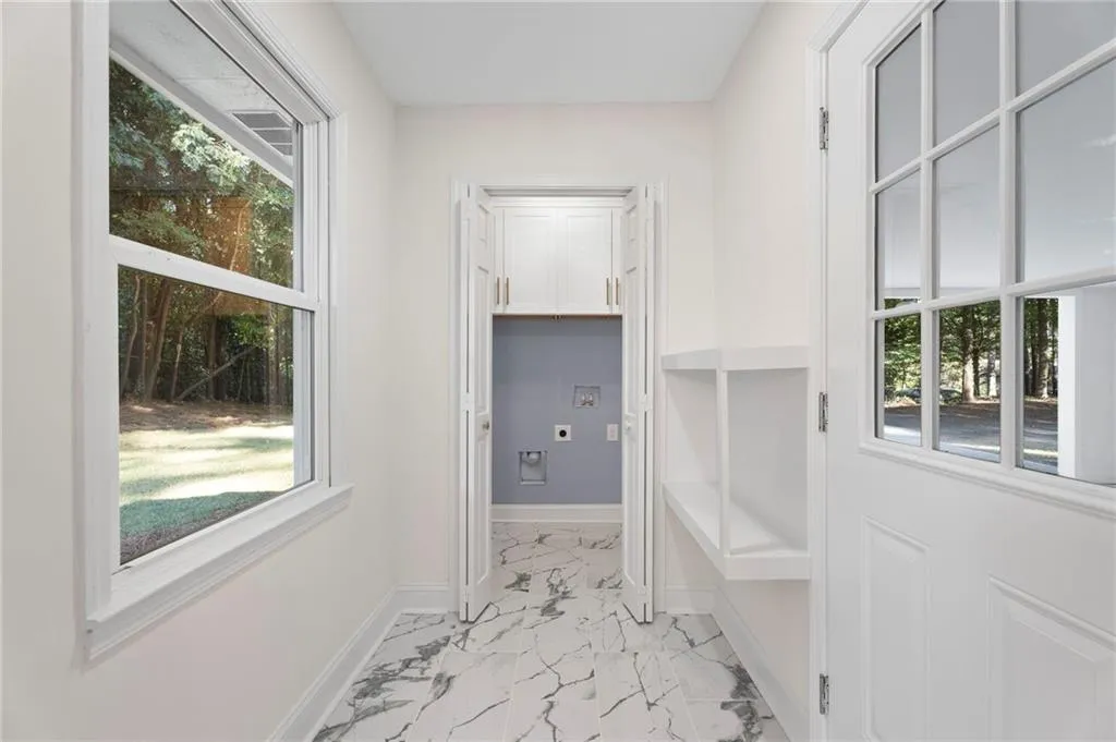 White paneled door with glass inserts, built-in shelving, white walls, large window, and marbled tile flooring