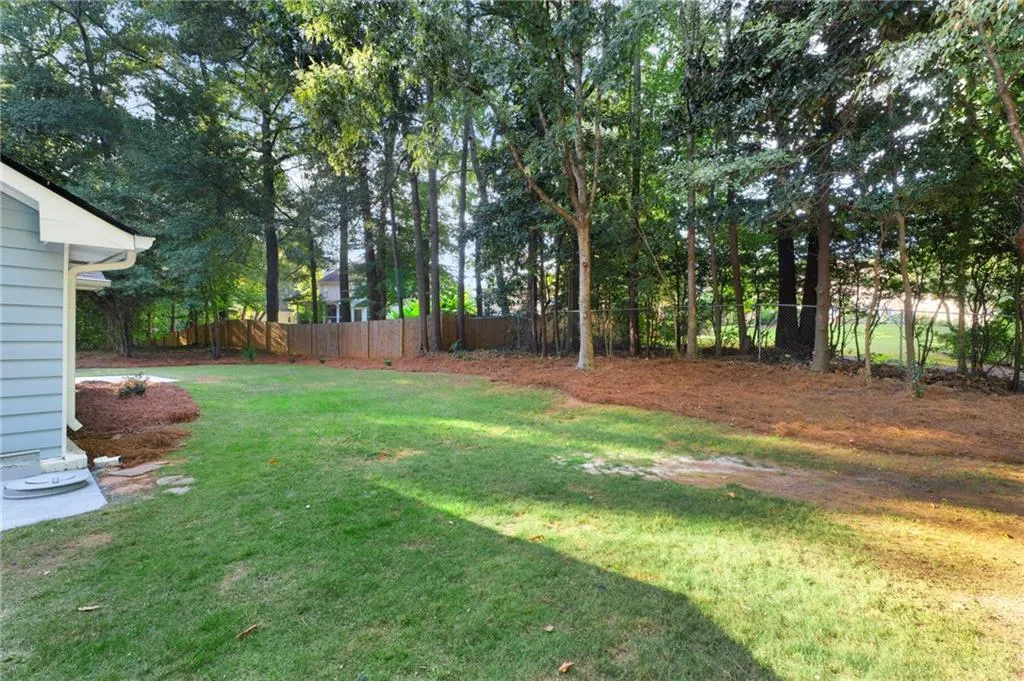 Expansive backyard featuring a manicured lawn, established perimeter trees, wood privacy fencing, and pine straw landscaping