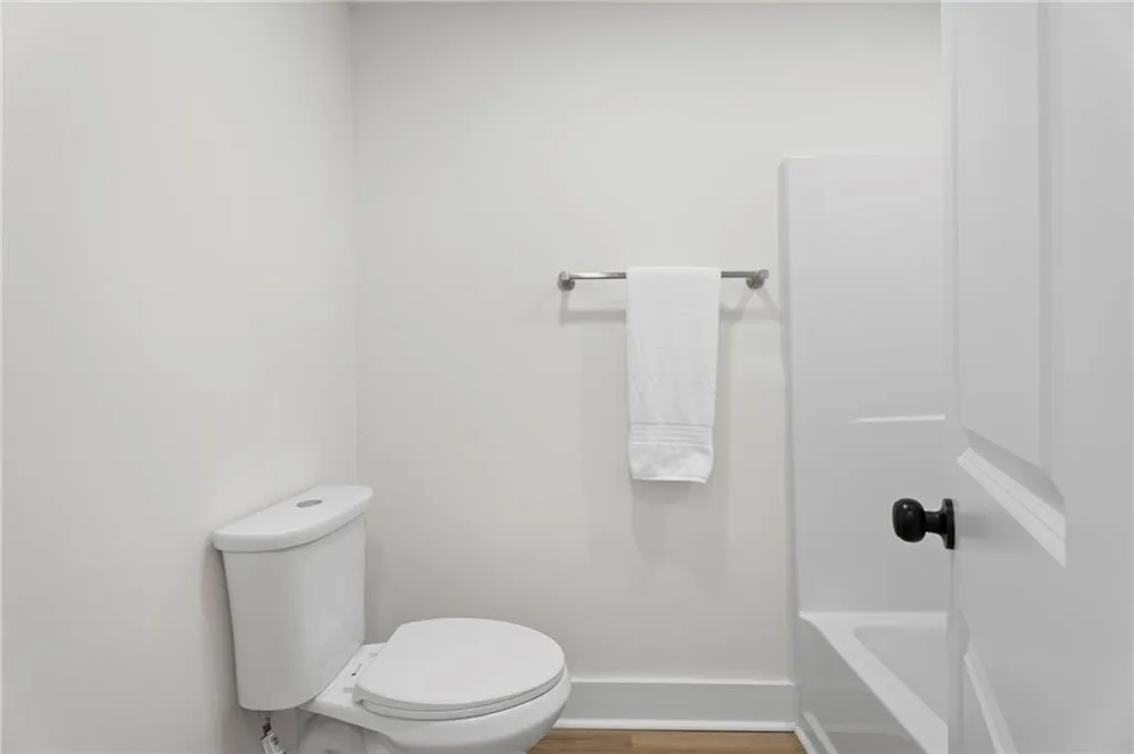 White toilet, wood-finish flooring, white walls, and a towel bar