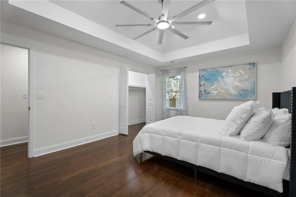 Tray ceiling with recessed lighting, ceiling fan, wood-finish flooring, and a window with sheer curtains