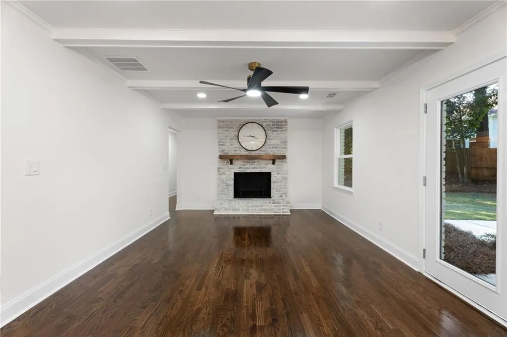 Spacious open-concept living area showcasing rich wood-finish flooring, recessed ceiling detail with ceiling fan, and a striking focal-point fireplace with white surround and integrated mantel
