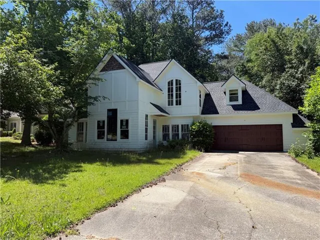 Two-story exterior with white siding, a dark shingle roof, a two-car garage with a wood-look door, an arched multi-pane window, and a dormer window