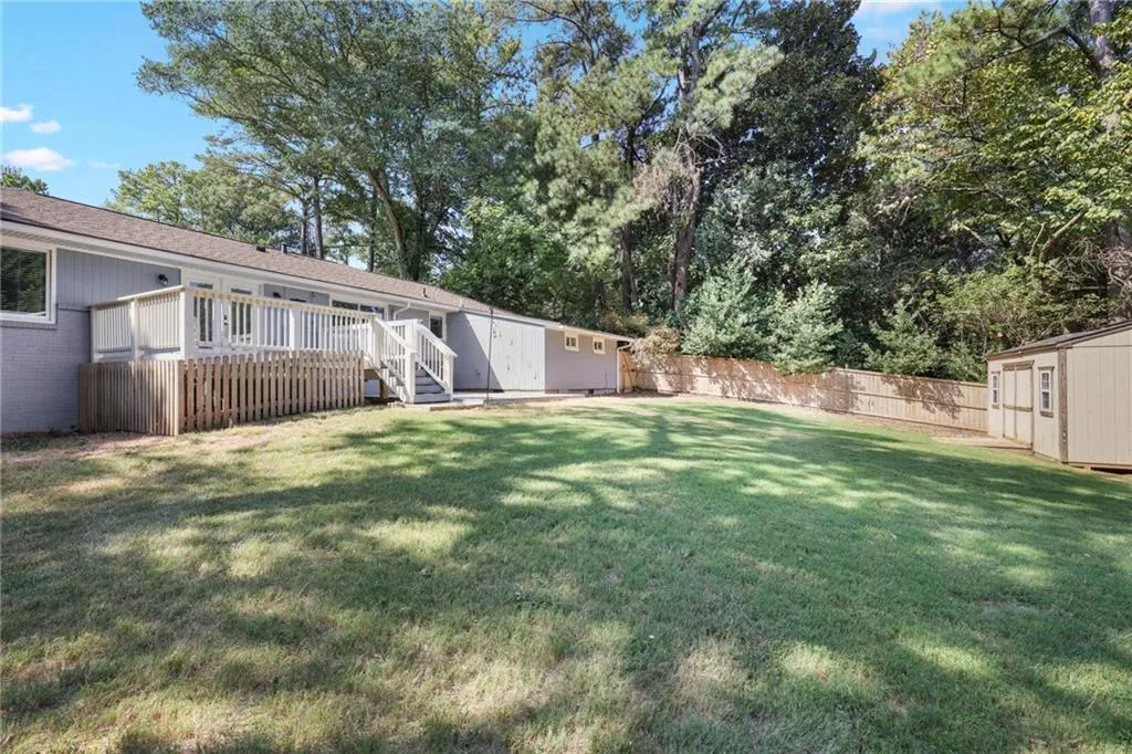Fenced backyard featuring a shed, a deck, and view of wooded area Fenced backyard featuring a shed, a deck, and view of wooded area