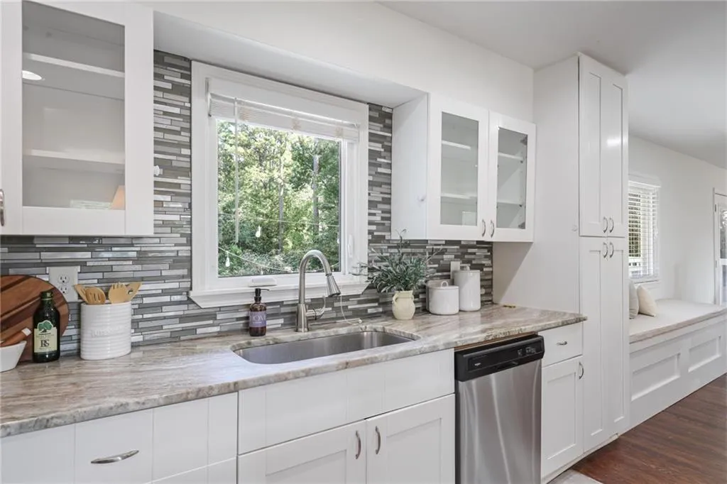 Kitchen with glass insert cabinets, tasteful backsplash, white cabinetry, and stainless steel dishwasher Kitchen with glass insert cabinets, tasteful backsplash, white cabinetry, and stainless steel dishwasher