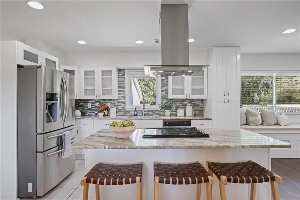Kitchen featuring stainless steel fridge with ice dispenser, a kitchen bar, light stone countertops, white cabinetry, and backsplash Kitchen featuring stainless steel fridge with ice dispenser, a kitchen bar, light stone countertops, white cabinetry, and backsplash