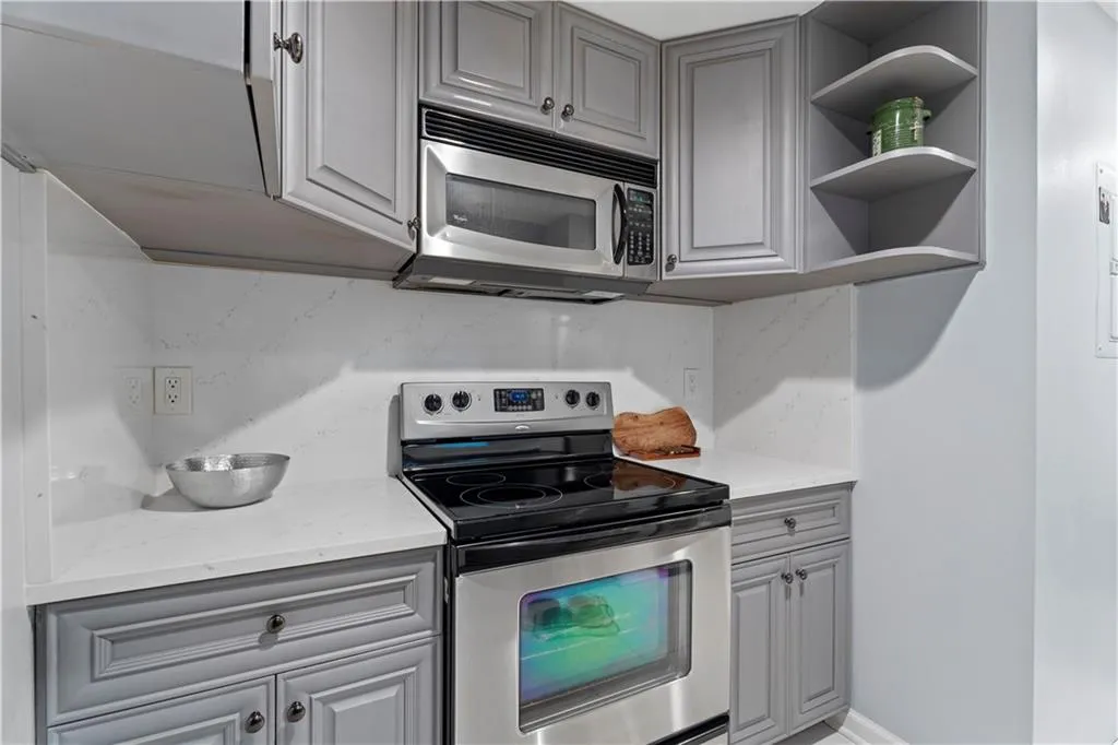 Kitchen with gray cabinets, appliances with stainless steel finishes, open shelves, and light stone counters