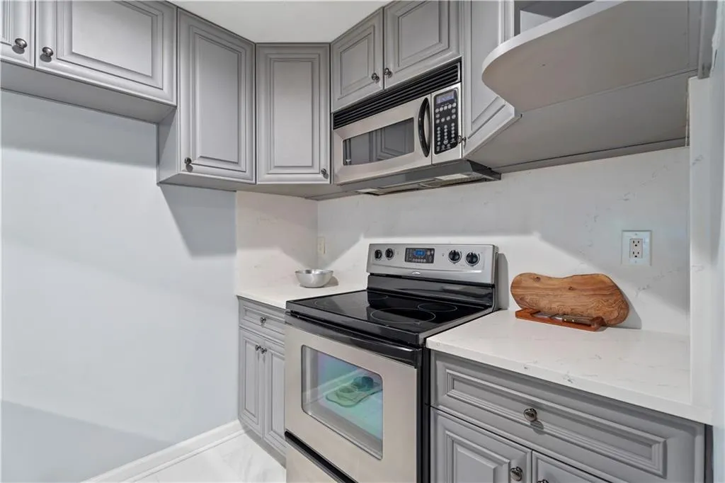 Kitchen featuring gray cabinetry, stainless steel appliances, light stone counters, and light marble finish flooring