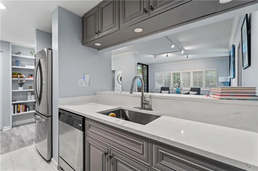 Kitchen with appliances with stainless steel finishes, track lighting, light stone countertops, gray cabinets, and crown molding