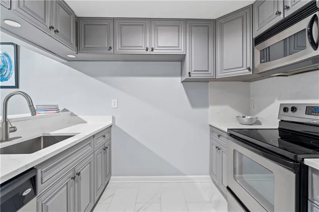 Kitchen featuring gray cabinets, appliances with stainless steel finishes, light marble finish flooring, and light stone countertops