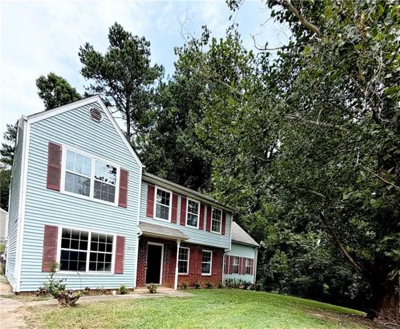 Two-story residence featuring light blue siding with red shutters and a brick facade