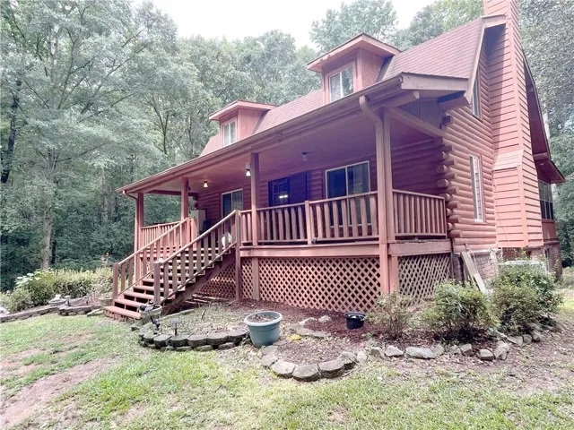Log cabin exterior with a covered porch, wood railing, and dormer windows