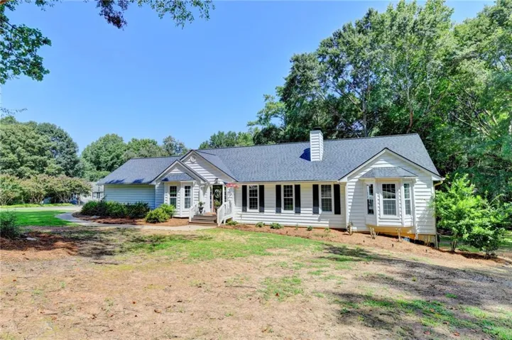 White siding exterior with a dark shingle roof, chimney, bay window, and covered entry porch