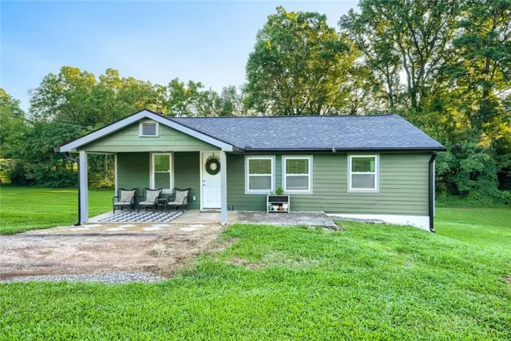 Green exterior siding, covered front porch, white front door, multiple windows, dark shingle roof