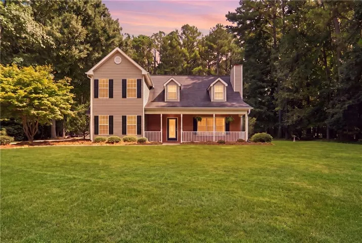 Expansive front lawn with mature landscaping, a covered front porch, and dormer windows
