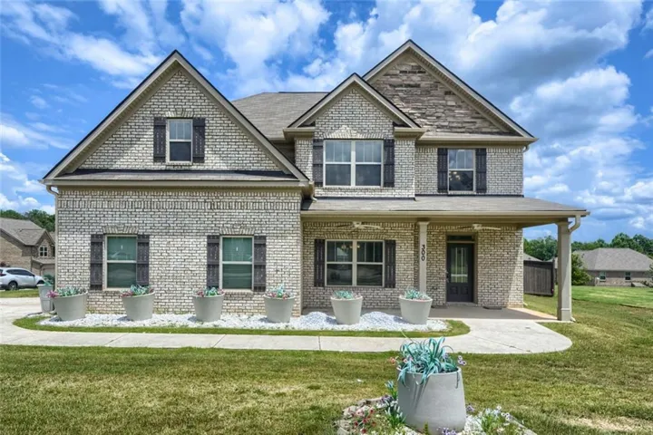 Two-story brick exterior featuring gabled rooflines, dark shutters, an inviting covered porch, and a concrete walkway