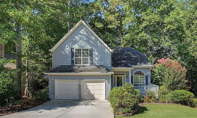 Two-car garage, arched window accents, mature trees, landscaped front yard, and a welcoming front porch