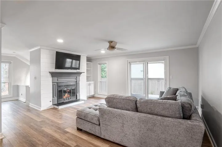 Living space featuring wood-finish flooring, a fireplace with a dark mantel and shiplap surround, built-in shelving, and a ceiling fan