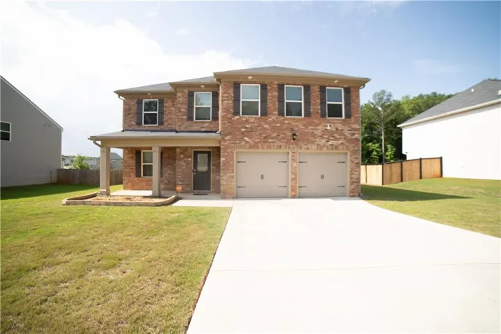 Brick facade residence featuring a covered front porch, a two-car garage, a concrete driveway, and a manicured lawn