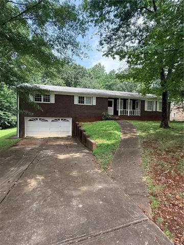 Brick ranch home featuring a two-car garage with white panel doors, covered front porch with white railings, and multiple windows with white trim