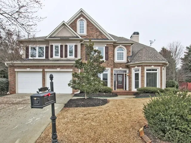 Brick facade residence featuring a two-car garage, multiple gables, an arched window, and a prominent bay window