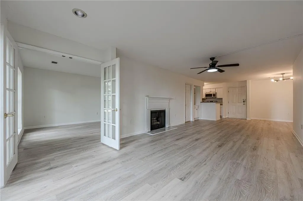 Unfurnished living room featuring french doors, a fireplace with raised hearth, light wood-type flooring, and ceiling fan