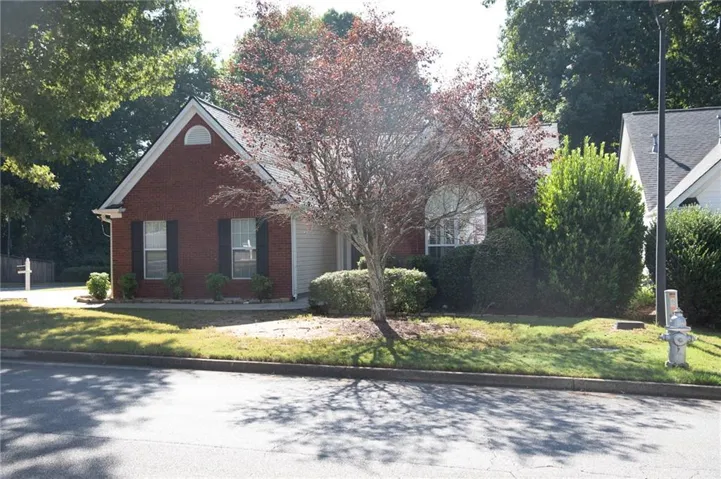 Brick exterior featuring a gabled roofline, arched window, and landscaped front yard with mature trees