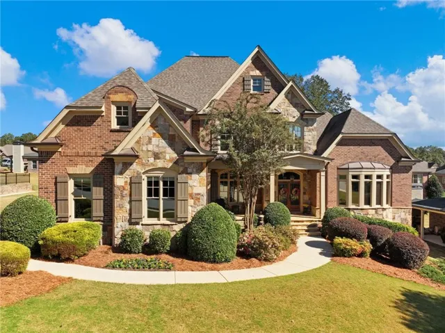 French country style house with stone siding, brick siding, a front yard, and a shingled roof
