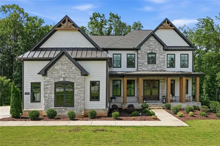 Stone and siding exterior with dark-framed windows, a covered entry porch, wood columns, and a landscaped front yard