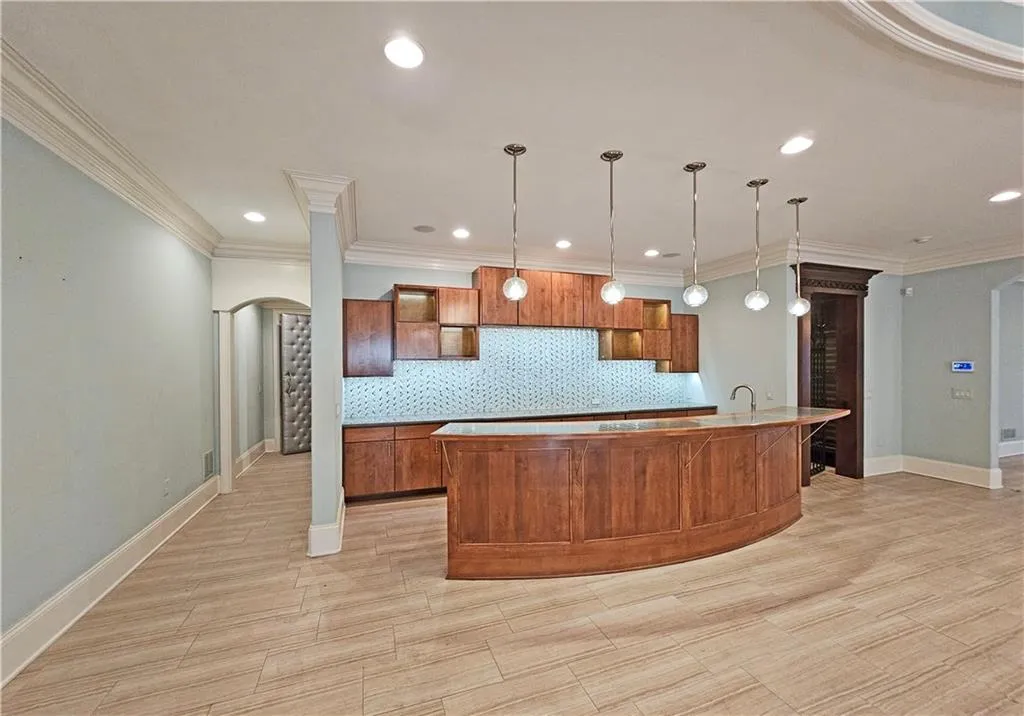 Kitchen featuring backsplash, crown molding, sink, decorative light fixtures, and an island with sink
