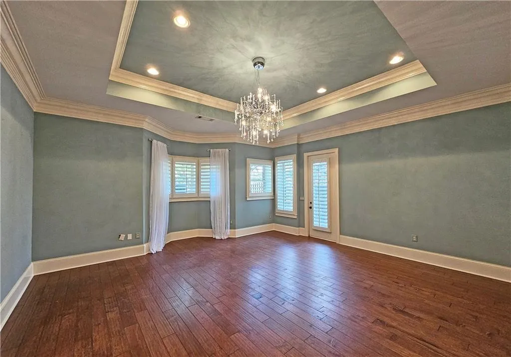 Empty room featuring a chandelier, a tray ceiling, and dark wood-type flooring