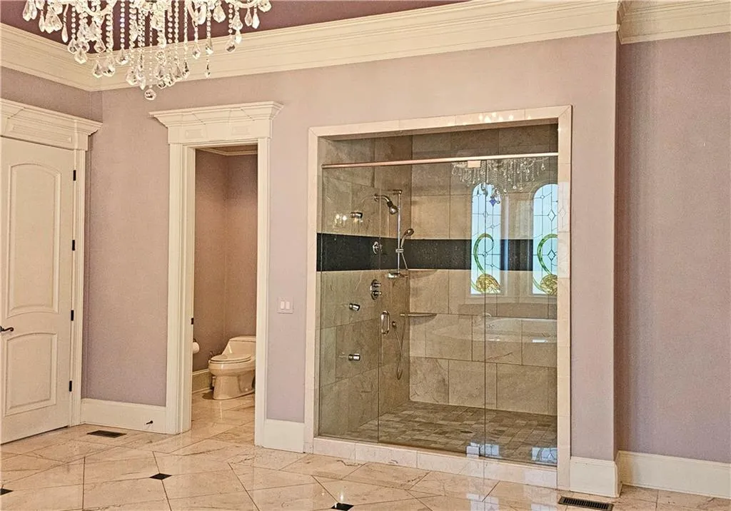 Bathroom with ornamental molding, tile flooring, an enclosed shower, an inviting chandelier, and toilet