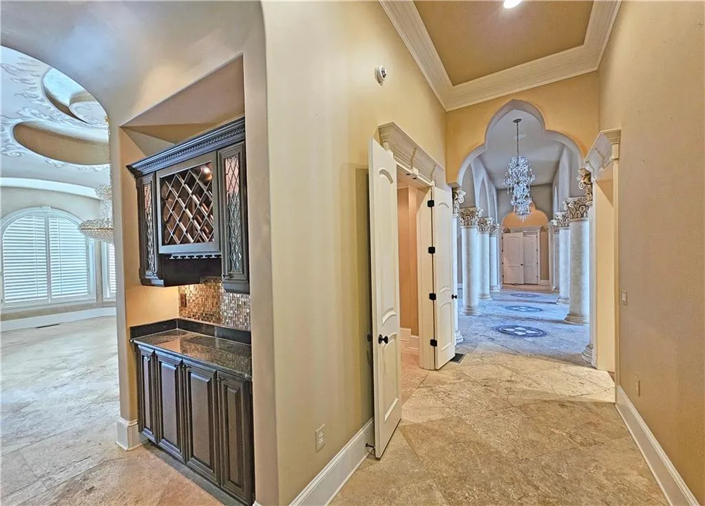 Hallway with a notable chandelier, ornamental molding, and light tile flooring