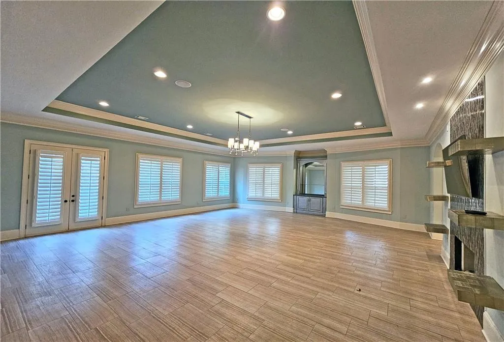 Unfurnished living room with an inviting chandelier, crown molding, french doors, and a raised ceiling