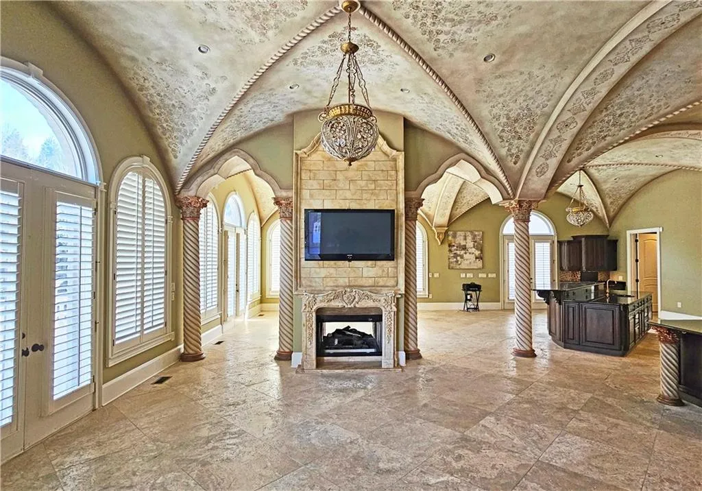 Unfurnished living room featuring a notable chandelier, plenty of natural light, a stone fireplace, and light tile floors