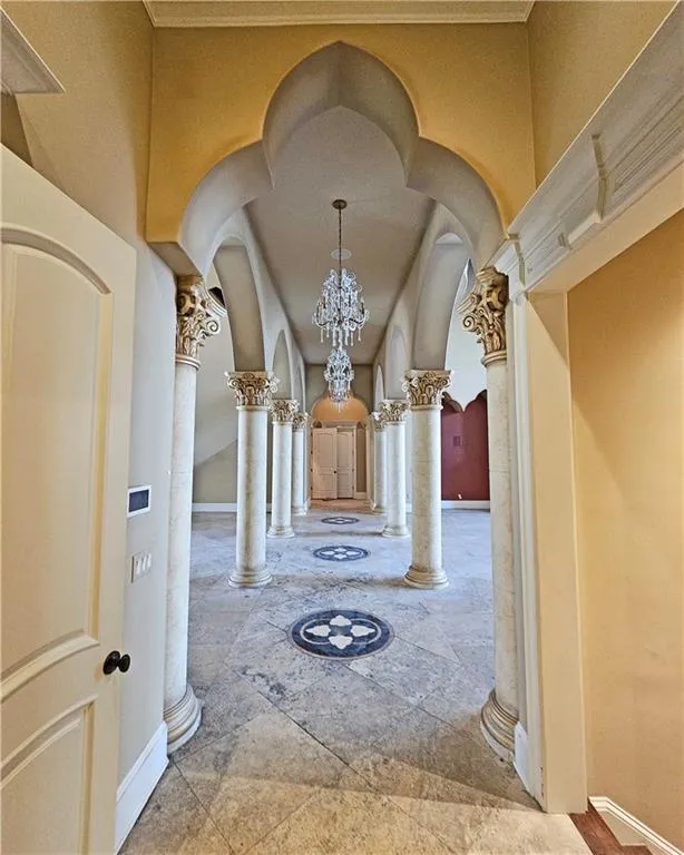 Hall featuring light tile flooring, a chandelier, and ornate columns