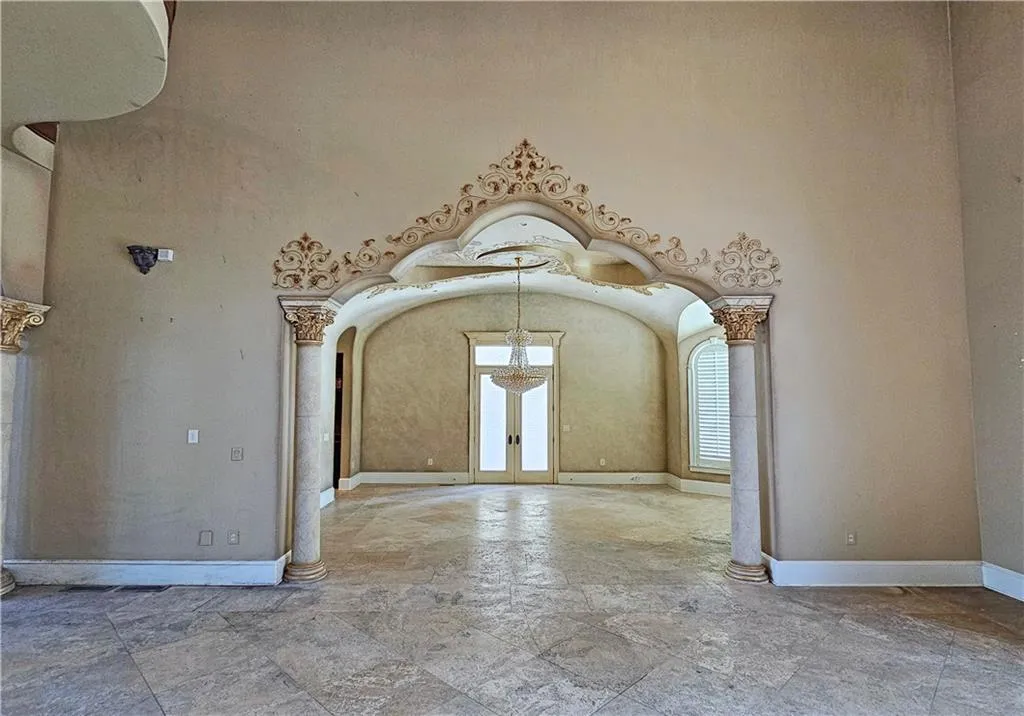 Spare room with an inviting chandelier, a towering ceiling, light tile flooring, and ornate columns