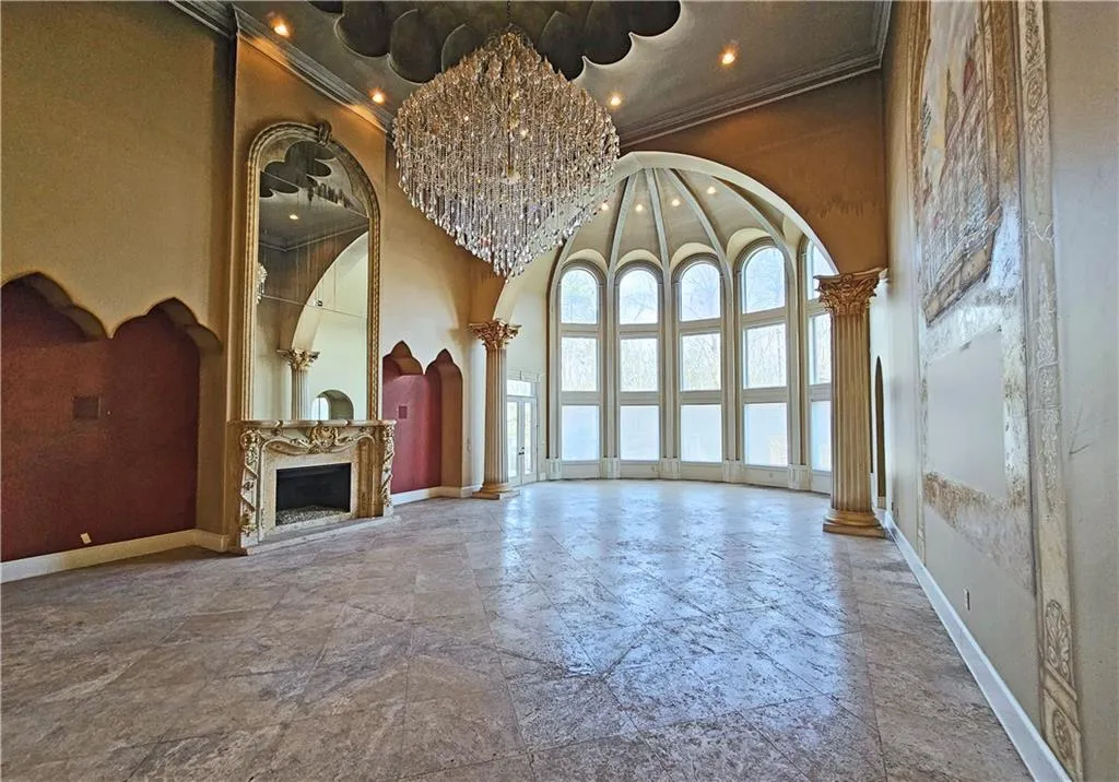 Unfurnished living room with a notable chandelier, tile floors, a towering ceiling, ornamental molding, and ornate columns