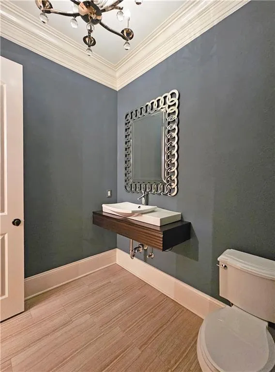 Bathroom featuring an inviting chandelier, ornamental molding, toilet, and wood-type flooring